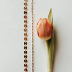 Rose gold chain necklace with a single tulip on a light background