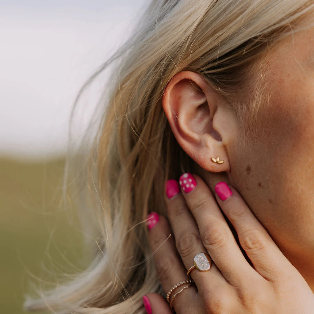 Close-up of a person's ear with an earring, hand with pink nail polish, and rings.