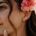 Close-up of a woman's ear with floral hair accessory and blue nail polish.