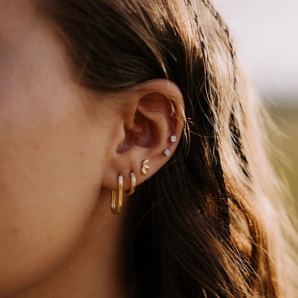 Close-up of an ear with gold hoop earrings and small stud earrings.