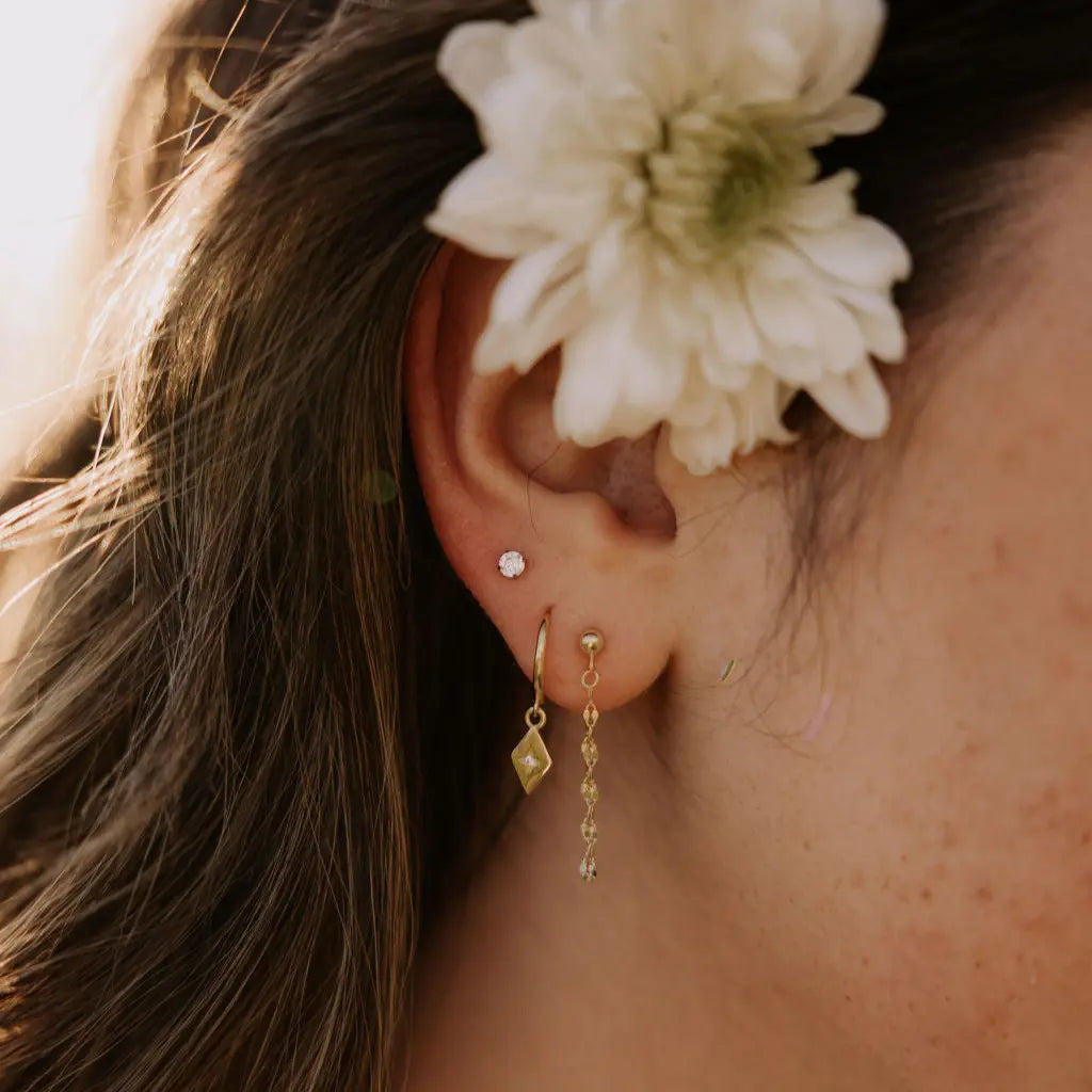 Close-up of an ear with gold earrings and a white flower in hair