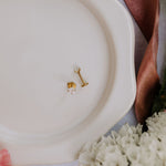 Gold earrings on a white plate with a brown napkin and floral decorations.
