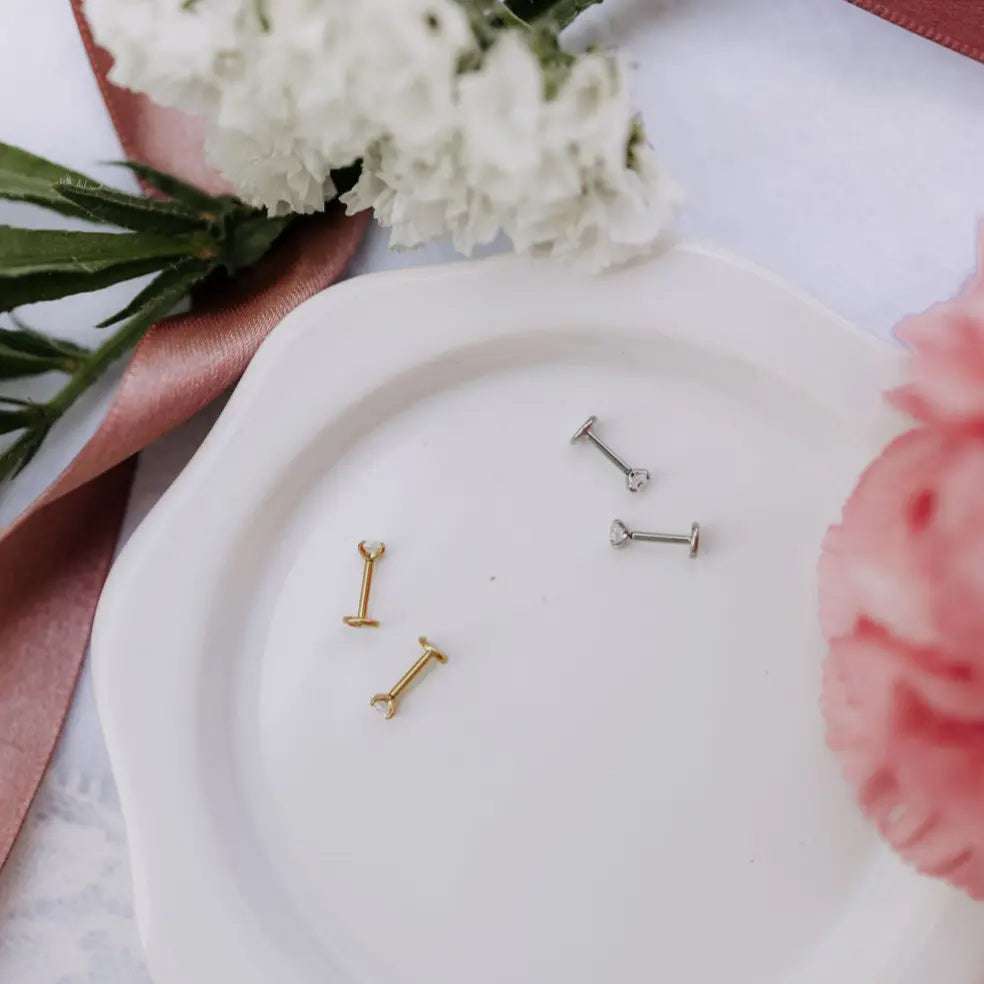Gold and silver earrings on a white plate with flowers and ribbons in the background