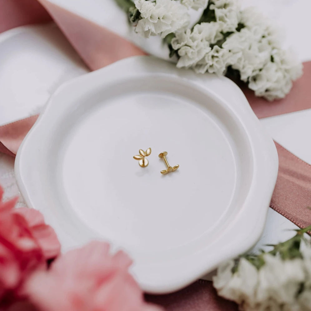 Gold earrings on a white dish with flowers in the background