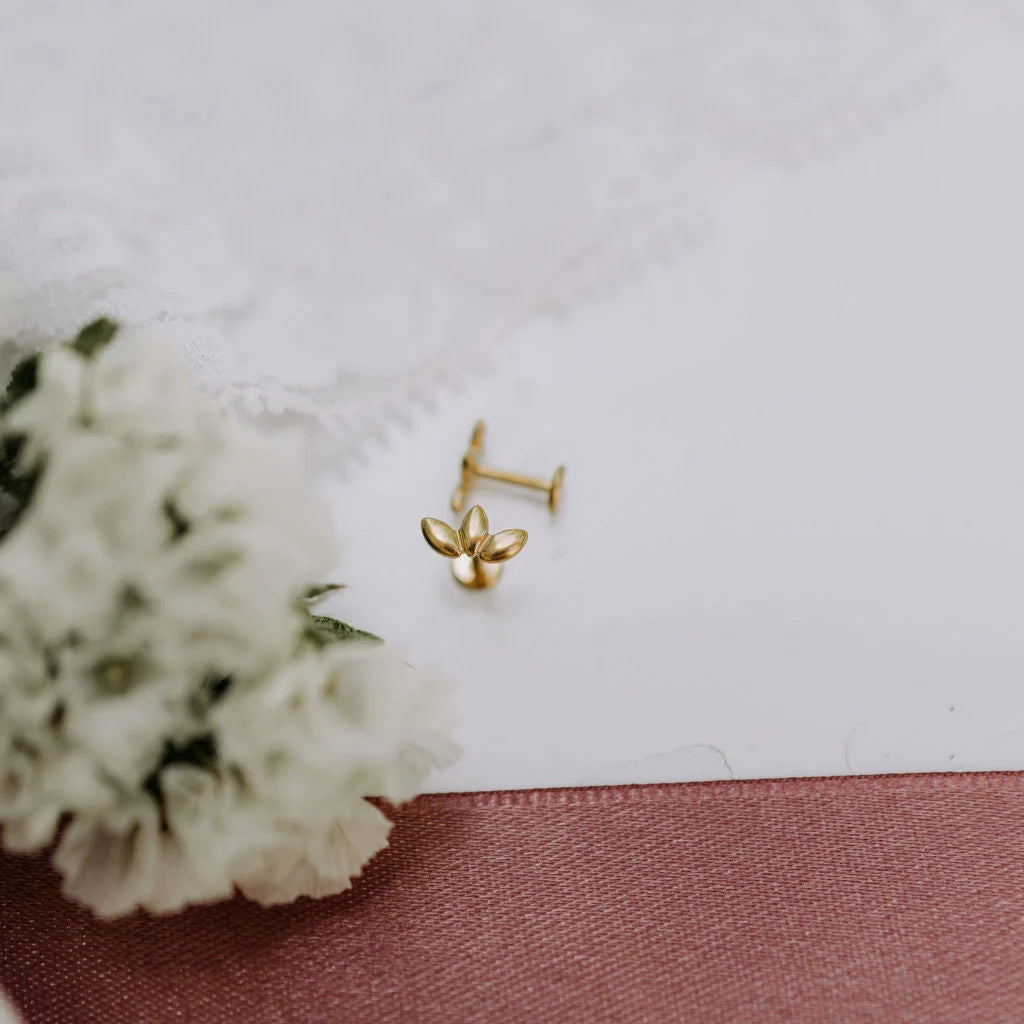 Gold earrings on a white surface with a pink ribbon and white flowers.