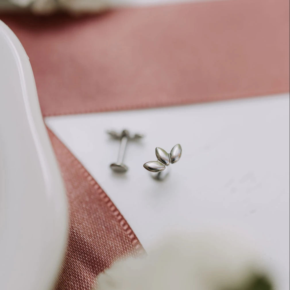 Silver leaf-shaped earrings on a white and pink fabric background