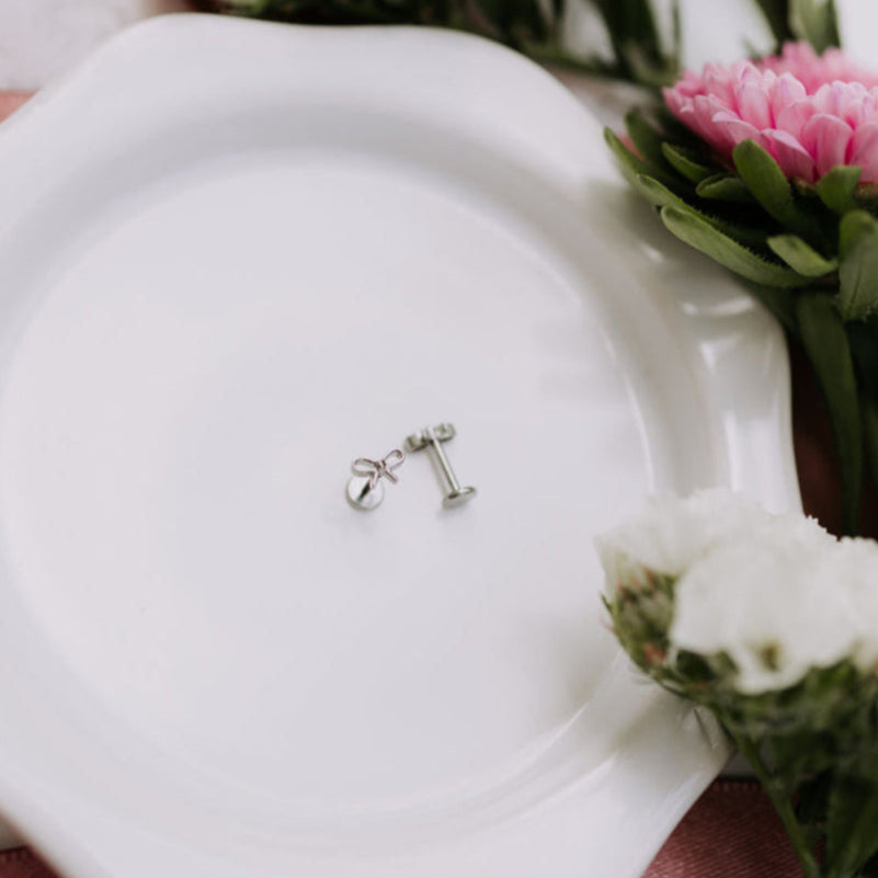 Silver earrings on a white plate with flowers in the background