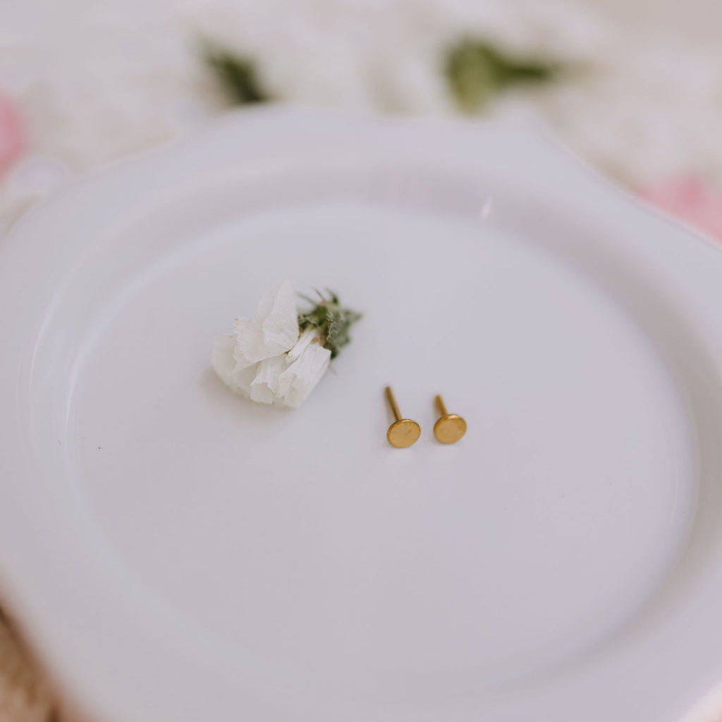Gold earrings on a white plate with a small bouquet of flowers.
