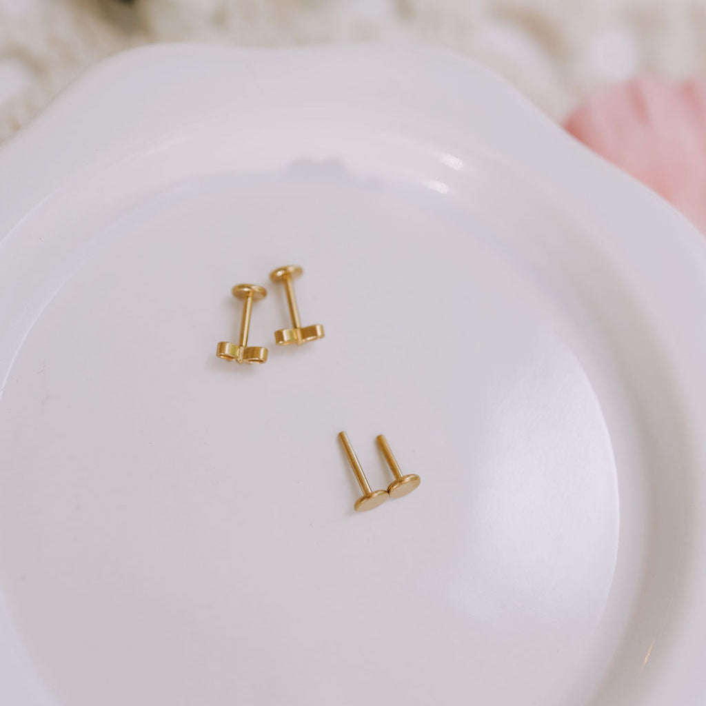 Gold earrings on a white dish with a soft, blurred background