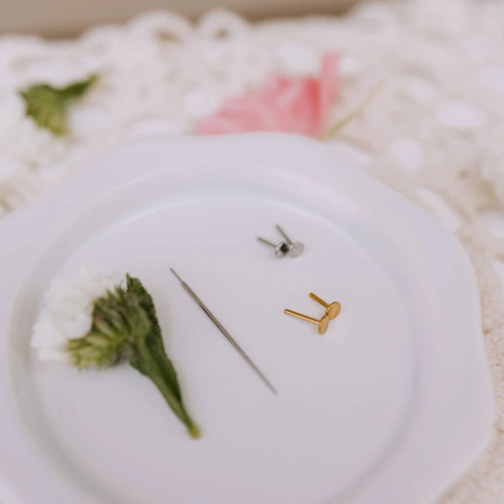Gold and silver earrings on a white surface with green leaves.