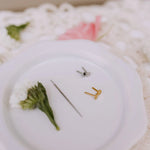Gold and silver earrings on a white surface with green leaves.