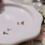 Gold and silver stud earrings on a white dish with a blurred background