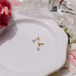 Gold earrings on a white plate with flowers in the background