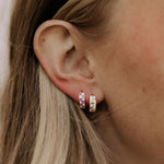 Close-up of an ear wearing two small hoop earrings with a neutral background by a woman with blonde hair
