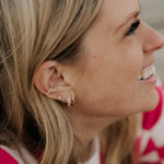 Close-up of a woman's ear with earrings, wearing a pink and white patterned sweater