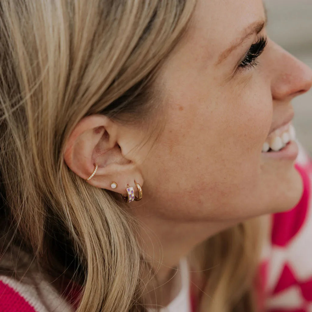 Close-up of a woman's ear with earrings, wearing a pink and white patterned sweater