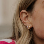 Close-up of an ear with multiple earrings against a neutral background
