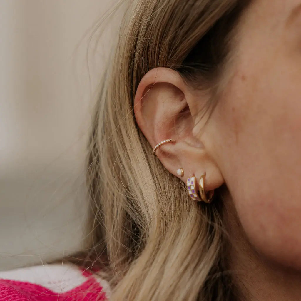 Close-up of an ear with multiple earrings against a neutral background