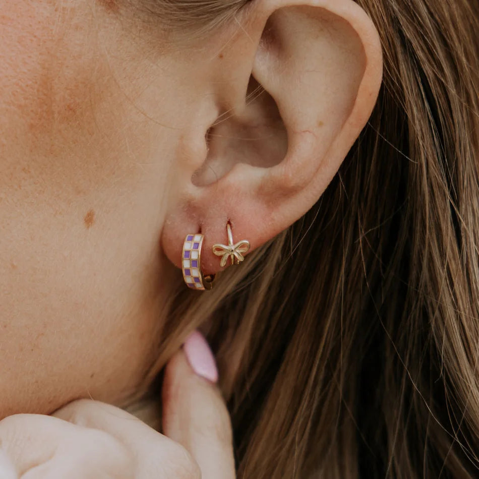 Close-up of an ear wearing gold hoop earrings with a bow detail.