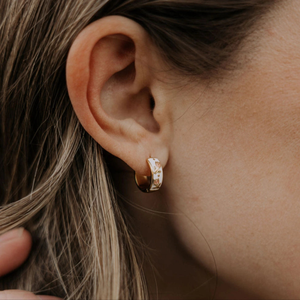 Close-up of an ear wearing a gold tulip hoop earring with a blurred background