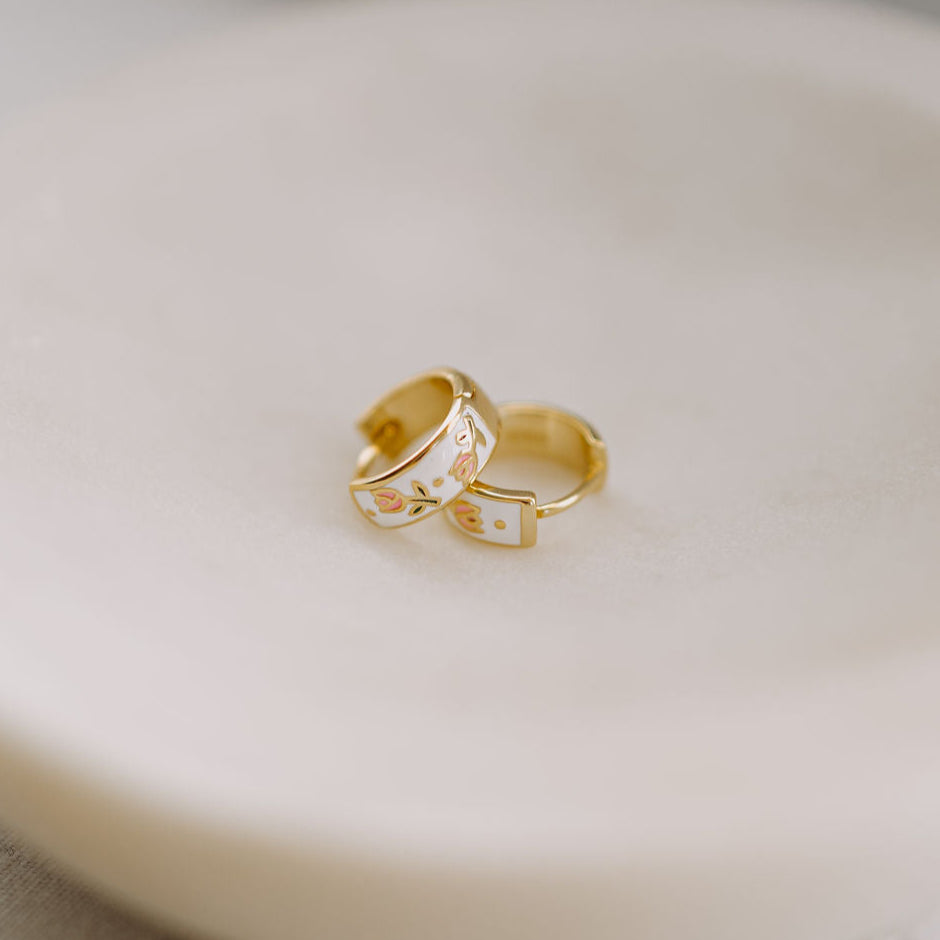Two gold earrings with small designs on a beige surface