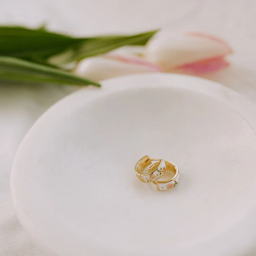 Gold earing on a white ceramic dish with tulips in the background