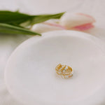 Gold earing on a white ceramic dish with tulips in the background