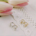 Gold and silver hoop earrings on a white lace doily with pink tulips in the background