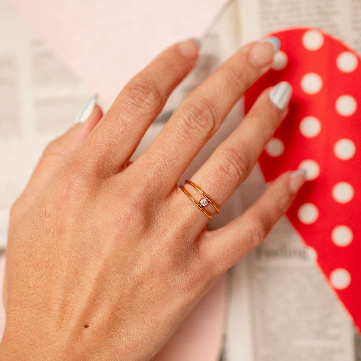 Hand wearing a ring with a red polka dot object in the background