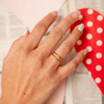 Hand wearing a ring with a red polka dot object in the background