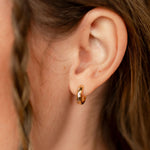 Close-up of a person wearing a gold hoop earring with braided hair.