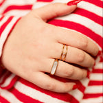 Load image into Gallery viewer, Hand wearing gold rings with a red and white striped shirt background
