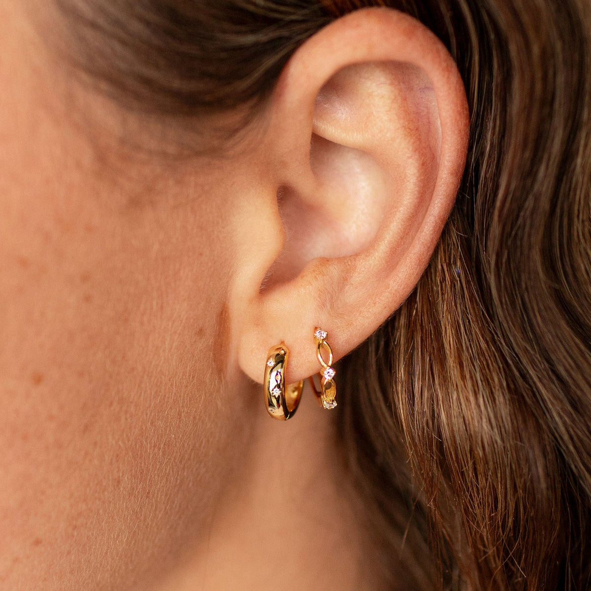 Close-up of a person wearing gold hoop earrings with a blurred background