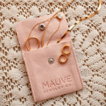 Gold earrings in a pink 'MAUVE JEWELRY CO.' pouch on a textured beige background