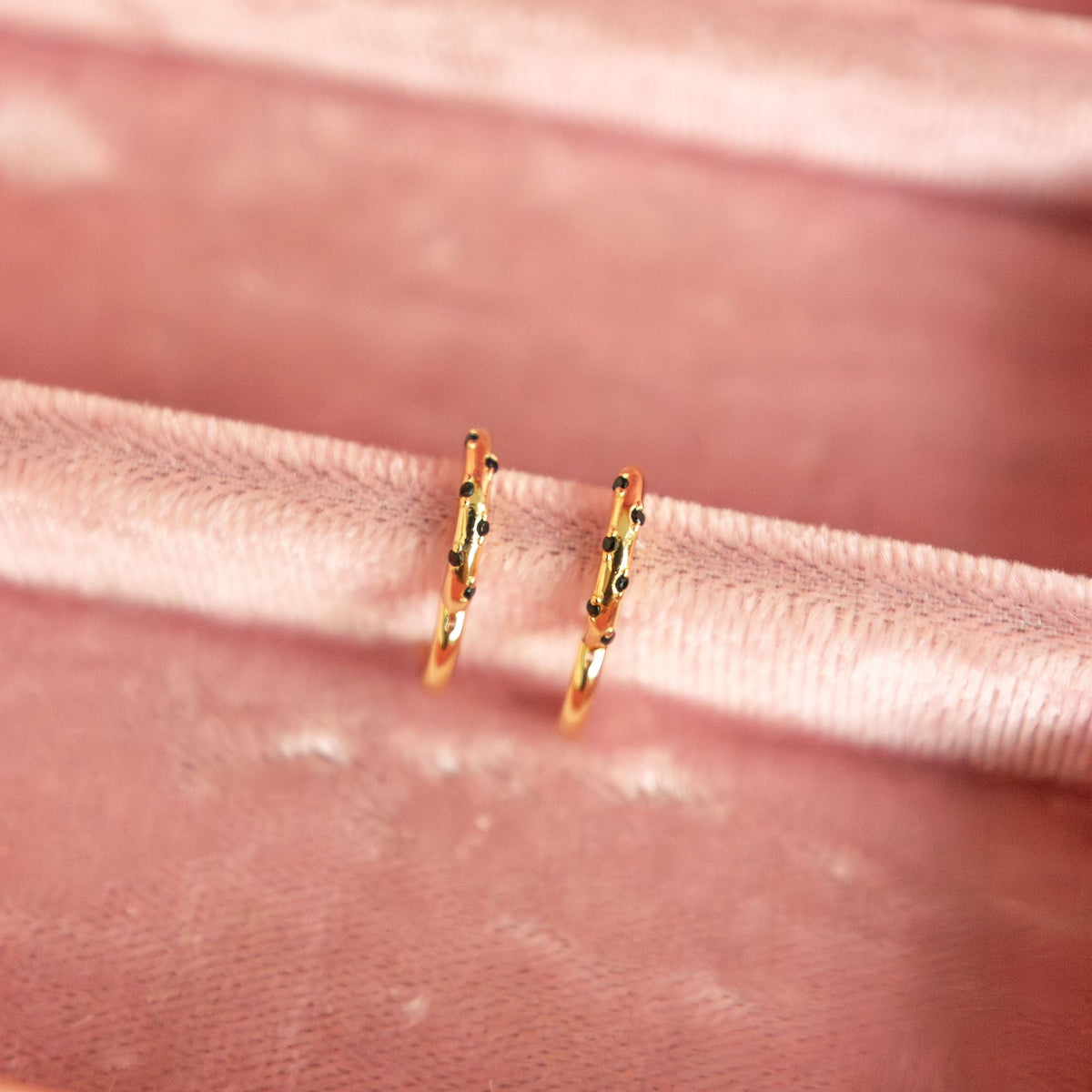 Gold hoop earrings on a pink velvet surface