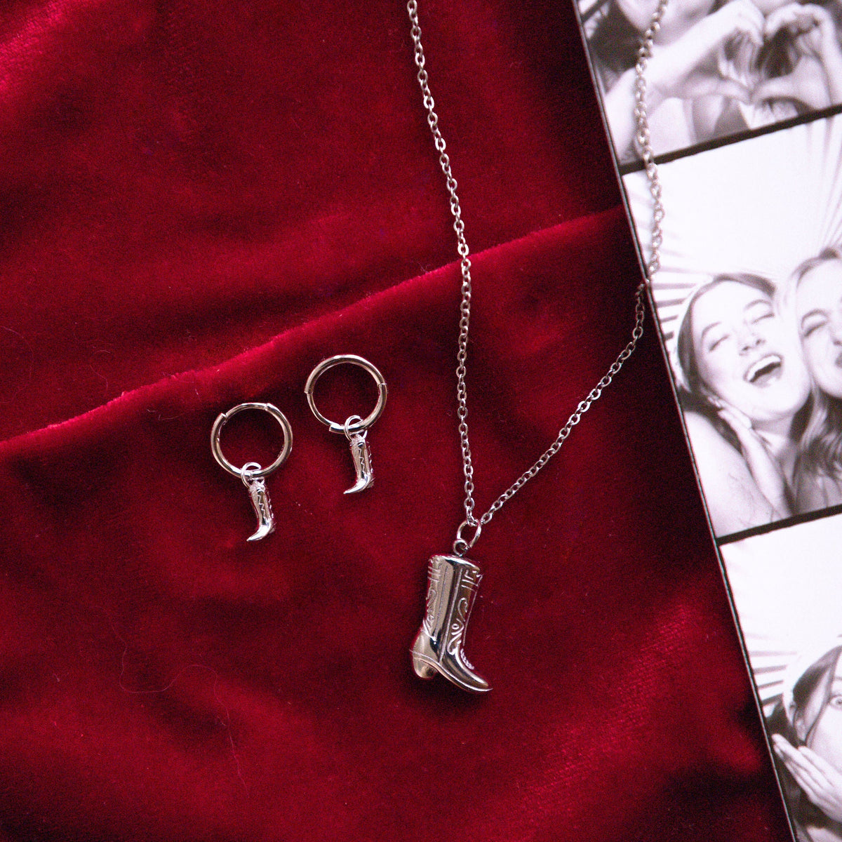 Silver necklace with cowboy boot and earring pendants on a red fabric background