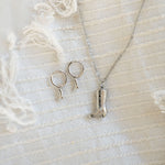 Silver boot hoops and boot necklace on white fabric background