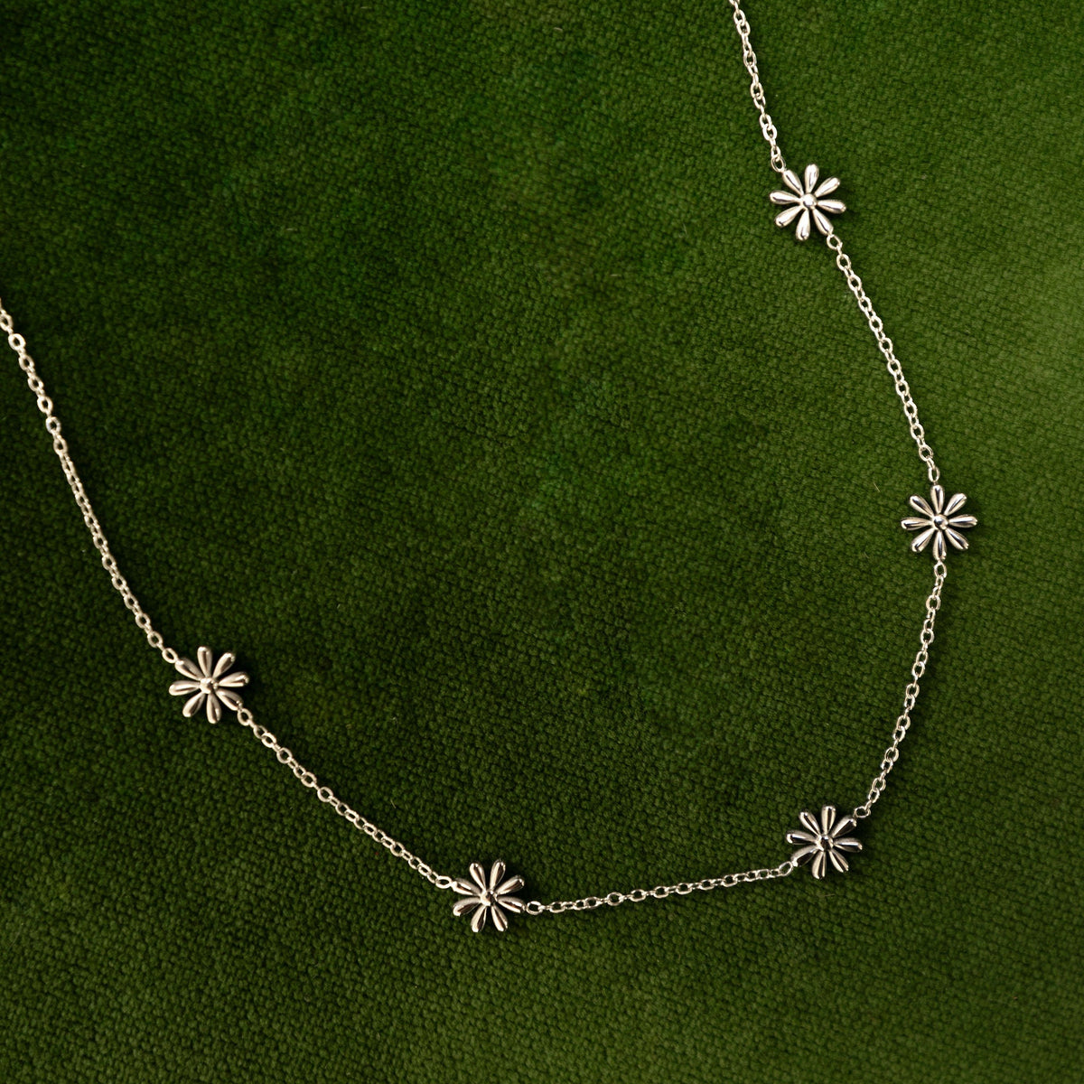 Silver necklace with flower shaped pendants on a green background