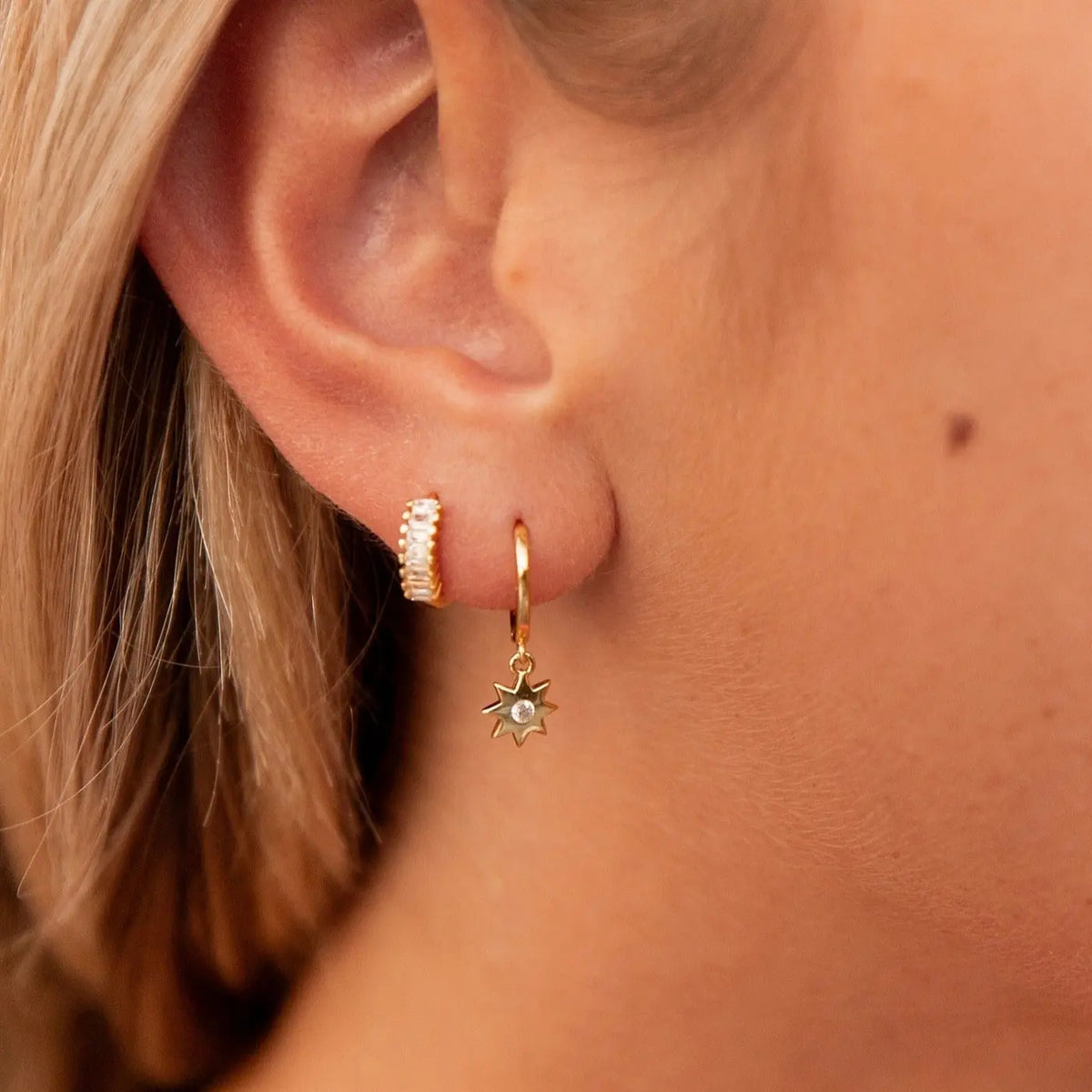 Close-up of a person wearing gold hoop earrings with sun and gemstone designs.