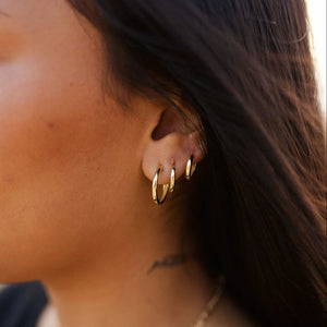 Close-up of an ear wearing gold hoop earrings with a blurred background