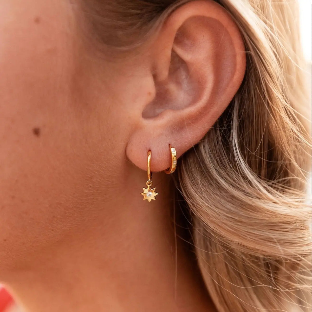 Close-up of a person wearing gold hoop earrings with sun-shaped charms.