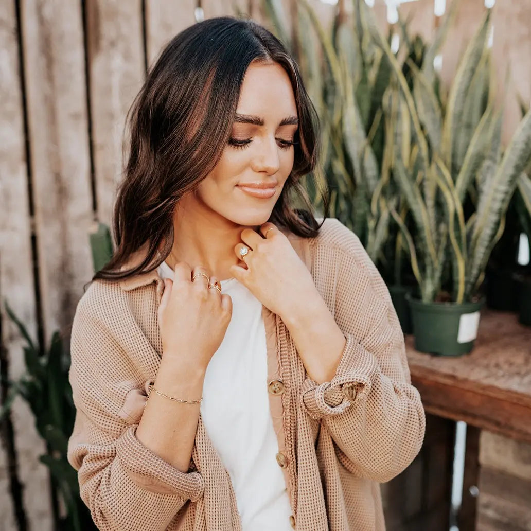 Woman adjusting her necklace outdoors with plants in the background