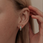 Close-up of a person wearing a small hoop earring and sunshine flat back stud with a hand adjusting it.