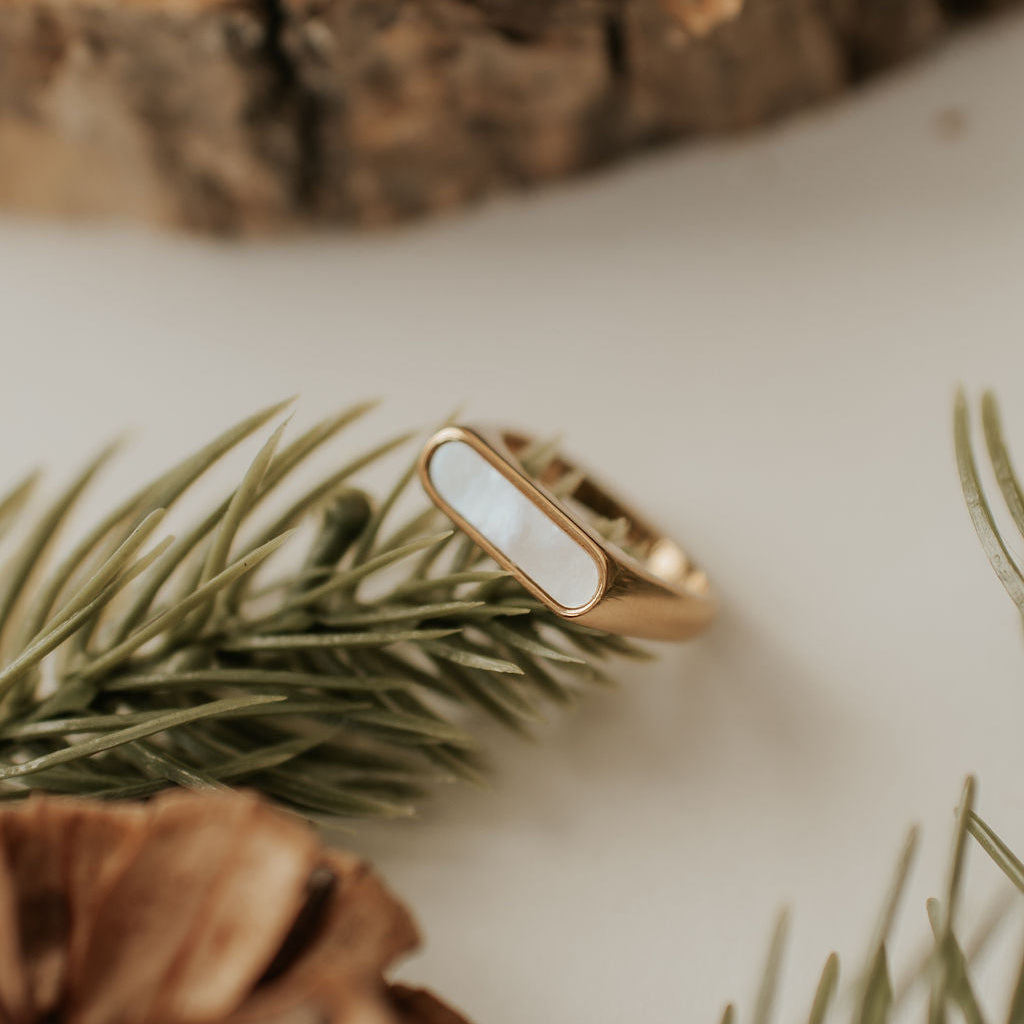 Gold ring with a white stone on a wooden surface with pine branches