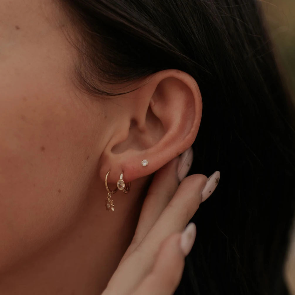 Close-up of an ear with gold hoop earrings and a hand touching the earlobe.