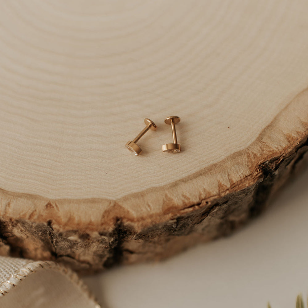 Gold stud earrings on a wooden surface with a neutral background