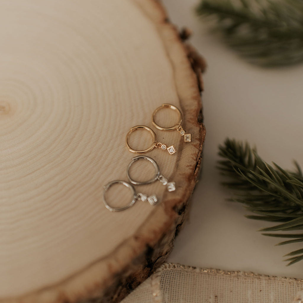 Gold earrings on a wooden surface with greenery