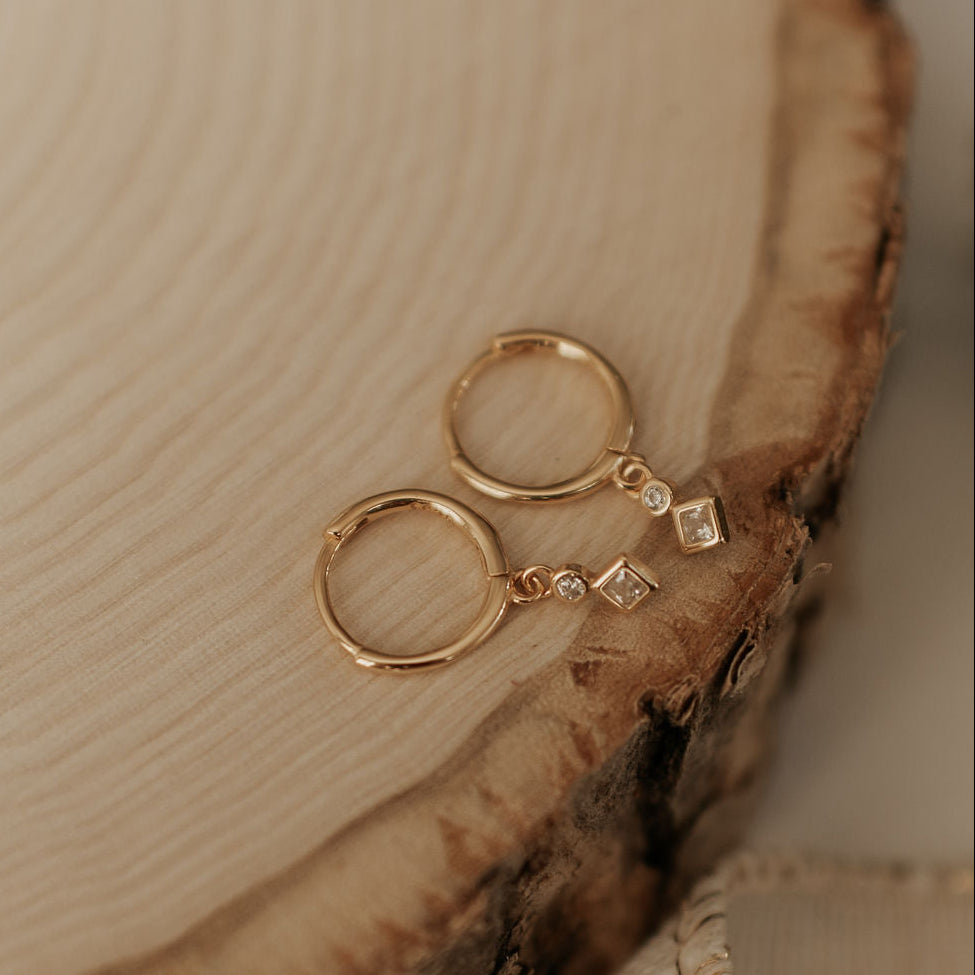 Gold hoop earrings with a small diamond on a wooden surface