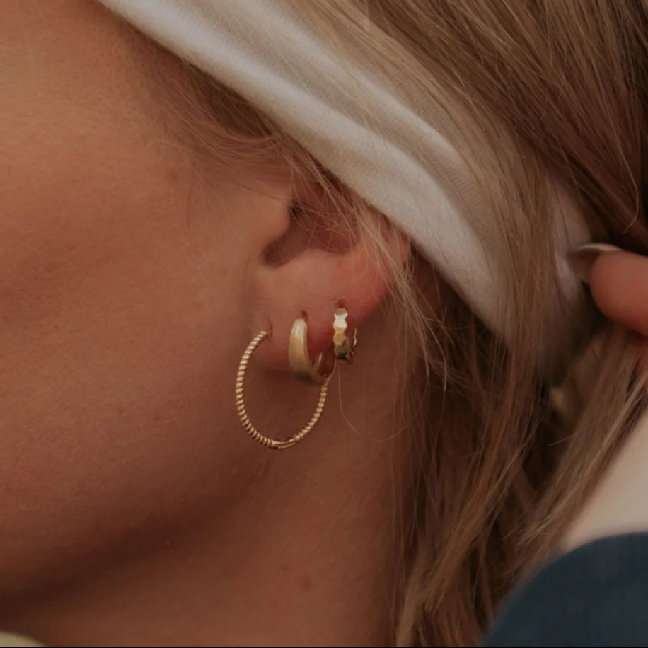 Close-up of a person wearing gold hoop earrings.