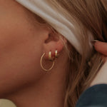 Close-up of an ear with gold hoop earrings and a white headband.